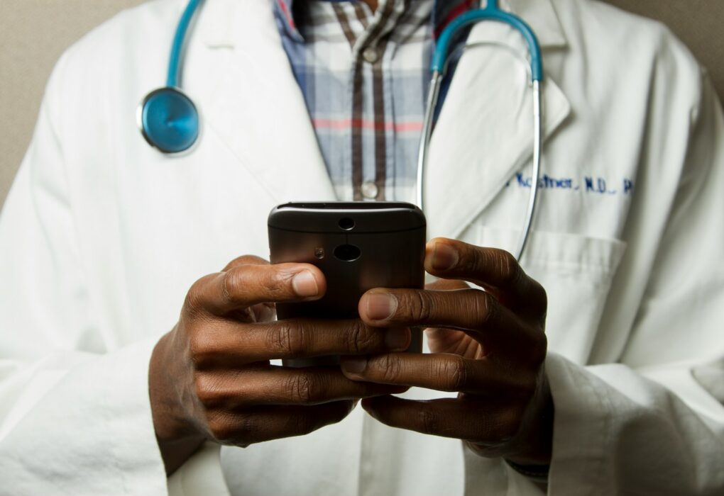 person wearing lavatory gown with green stethoscope on neck using phone while standing